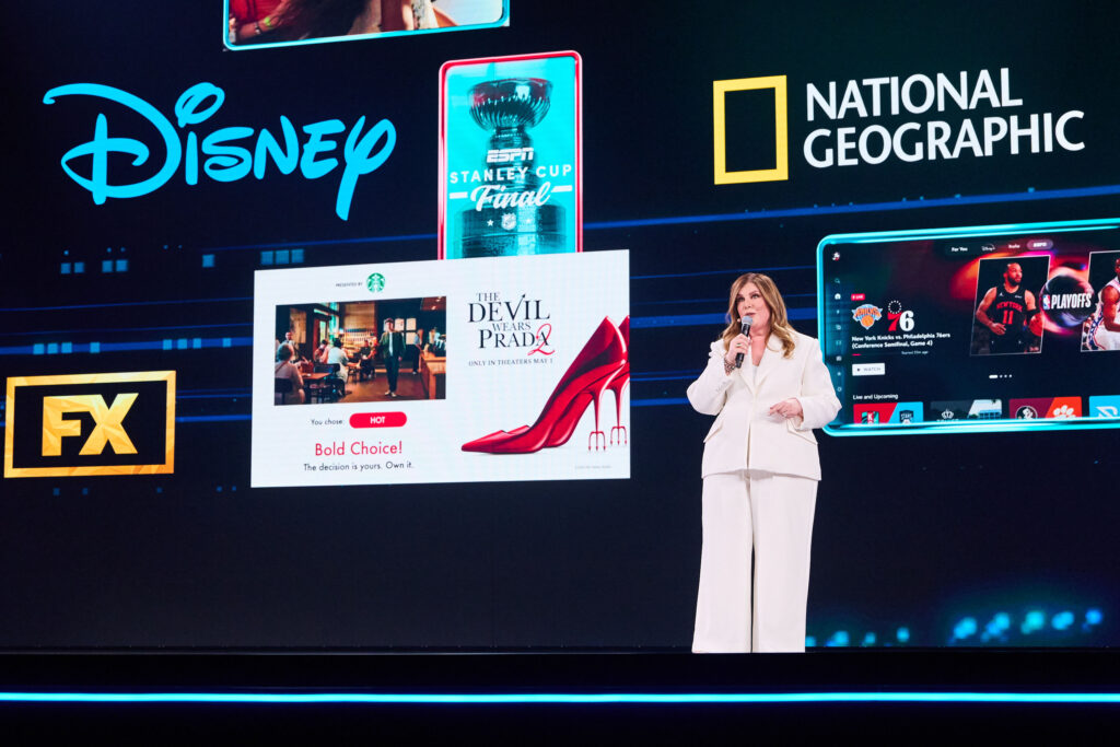 Female presenter on a stage with large screens displaying Disney, National Geographic, FX logos and ads for The Devil Wears Prada and ESPN Stanley Cup Final.